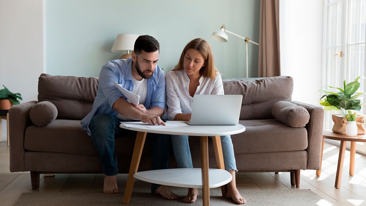 Una pareja milenaria seria se sienta en un sofá sellando papeles, revisando las facturas para gastos de servicios públicos, analizando impuestos, el pago de los hogares usa la aplicación de e-bank en una laptop. Gestionar el concepto de finanzas